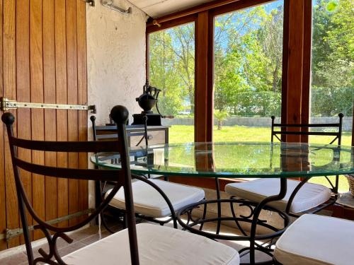 une table et des chaises en verre dans une pièce avec fenêtres dans l'établissement Maison 15 min plages, à Lairoux