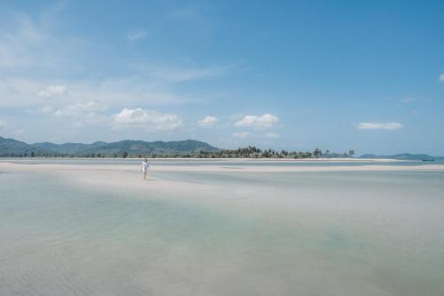 a person standing on a beach in the water at Six Senses Yao Noi in Ko Yao Noi