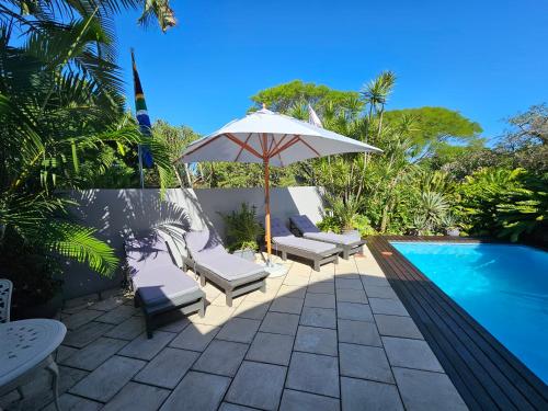 un patio con sombrilla, sillas y piscina en Leopard Corner Lodge en St Lucia