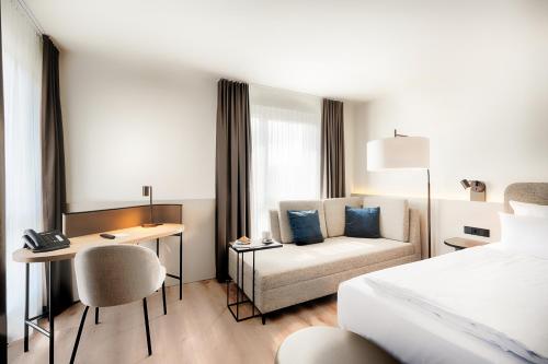 Welcome Hotel Darmstadt City Center في دارمشتات: غرفة الفندق بسرير ومكتب واريكة