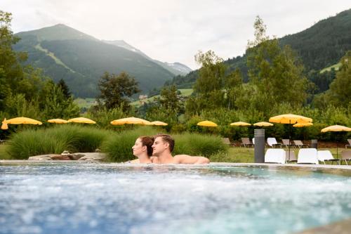 two women in a swimming pool with mountains in the background at Aktiv- & Gesundheitsresort das GXUND - Thermeneintritt inklusive in Bad Hofgastein