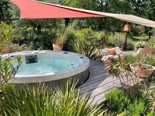 a hot tub in a garden with an umbrella at Maison d'Hôtes de Charme Le Clos de la Fontaine Piscine & SPA in Labastide-Marnhac