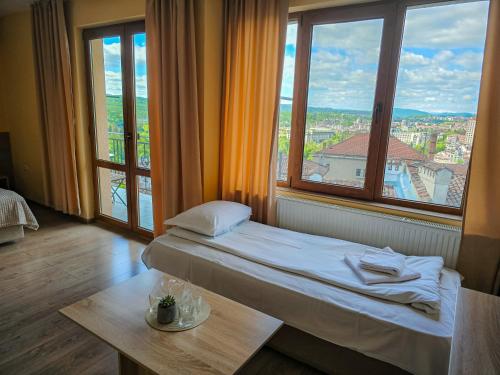 a room with a bed and a table and windows at Family Hotel "Slavianska dusha" - FREE PARKING in Veliko Tŭrnovo