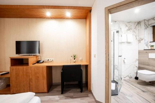 a room with a desk with a television and a bathroom at Hotel zum Buchenberg in Saint-Vith