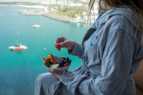 a woman holding a bowl of fruit with a view of the water at Hyatt Centric Jumeirah - Twin Room Sea View - UAE in Dubai