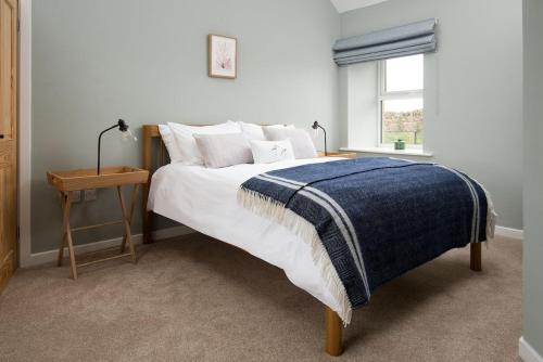 een slaapkamer met een bed met een blauwe deken en een raam bij The Rushes in Bamburgh