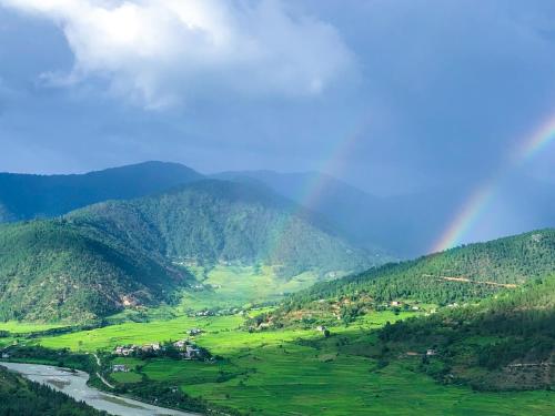 a rainbow over a green valley with a river at CheChey Village Homestay in Punākha