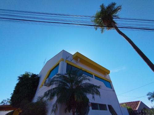 a white building with a yellow roof and a palm tree at Hotel Indi Suíte Standard in Ribeirão Preto