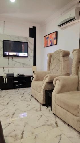 ein Wohnzimmer mit 2 Stühlen und einem Flachbild-TV in der Unterkunft J Lounge in Ikorodu