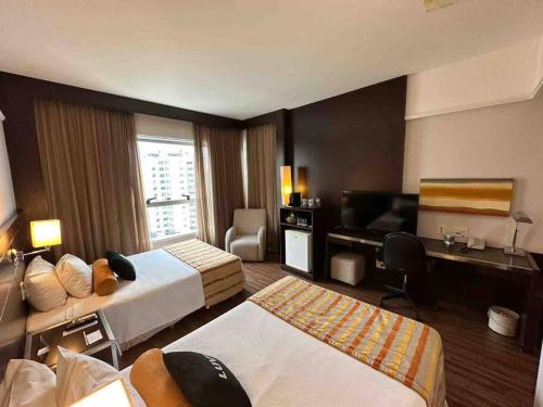 a hotel room with two beds and a desk at Suíte em hotel de luxo Savassi in Belo Horizonte