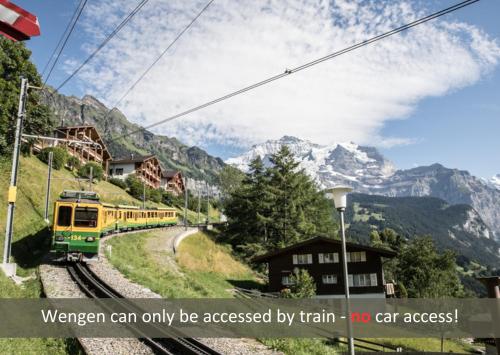 a train on the tracks with mountains in the background at Hotel Bellevue - Traditional Swiss Hideaway in Wengen