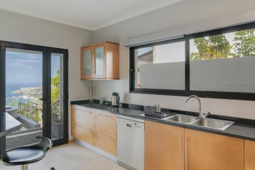 a kitchen with a sink and two large windows at Bay Bliss by Atlantic Holiday in Funchal