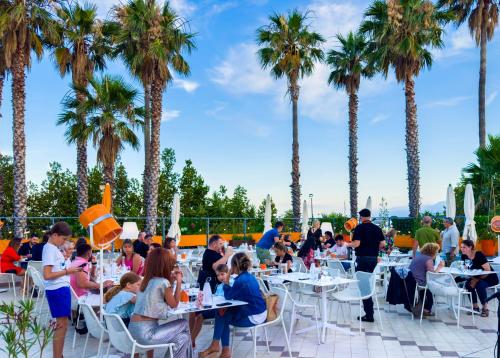 a group of people sitting at tables on a patio with palm trees at Ostella Spa & Resort in Bastia