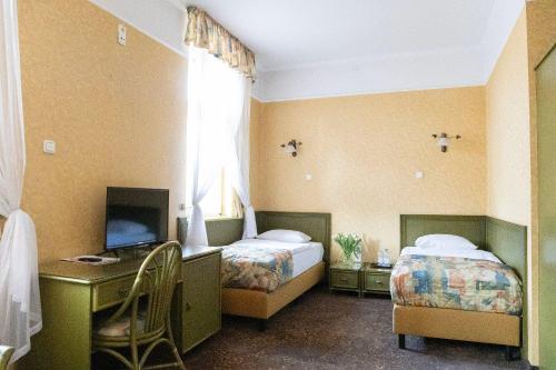 a bedroom with two beds and a desk and a television at Hotel Calisia in Kalisz