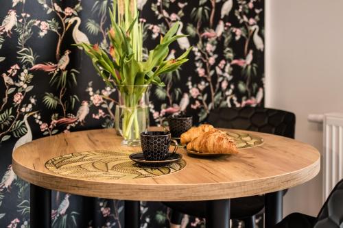 a wooden table with a vase of flowers and croissants at Heron - 77 Apartments Wigury - Dostęp na KOD - Parking - Smaczna Kawa - Centrum - Blisko Piotrkowska - Galeria - Widok na miasto - Klimatyzacja - 7 piętro - FV in Łódź