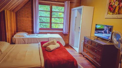 a bedroom with a bed and a tv and a window at Pousada Atalaia Capivari in Campos do Jordão