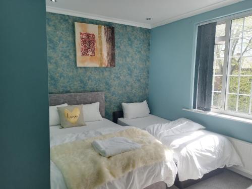 two beds in a bedroom with blue walls at An Exquisite Deluxe Room in a Hotel - Free Parking - with access to Resturant - Shisha Bar- Wine Bar in Roundhay