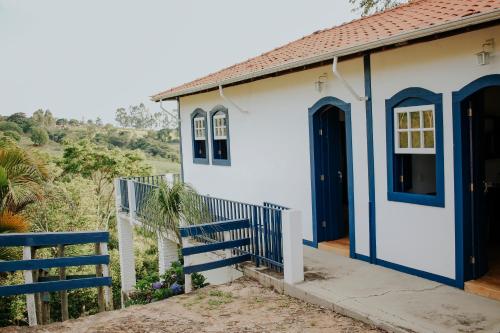 une petite maison blanche avec des portes bleues et une clôture dans l'établissement Recanto do Inconfidente, à Resende Costa