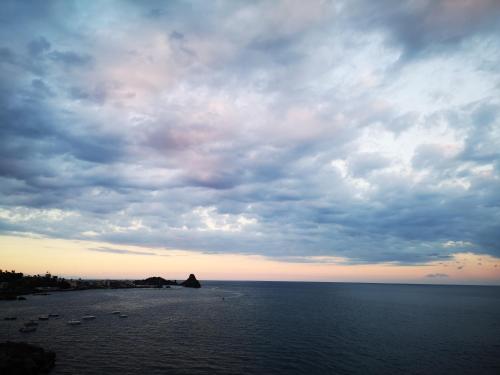 a cloudy sky over a body of water with boats at The sea you can feel in Aci Castello