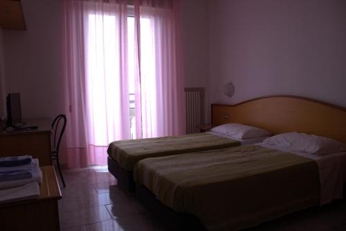 a bedroom with a bed and a window with pink curtains at Hotel Nord Ovest in Monte Grimano Terme