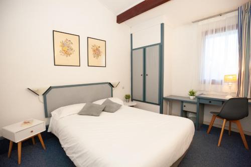 a bedroom with a white bed and a desk and a window at Hotel Atlantide in Biscarrosse