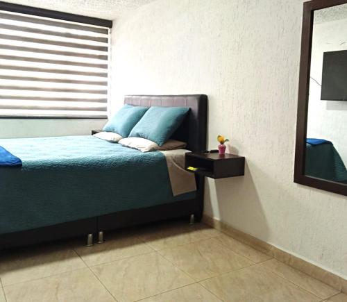 1 dormitorio con cama con almohadas azules y espejo en Habitación Hermosa iluminada, en Bogotá