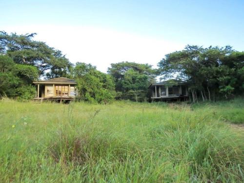 two houses in a grassy field with trees at Khangela Private Game Lodge - Self Catering - Bedrooms are 3 Separate Chalets - Hluhluwe in Hluhluwe