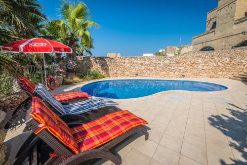 a pair of lounge chairs and an umbrella next to a swimming pool at 3 Bedroom Holiday Home with Private Pool and Views in Nadur
