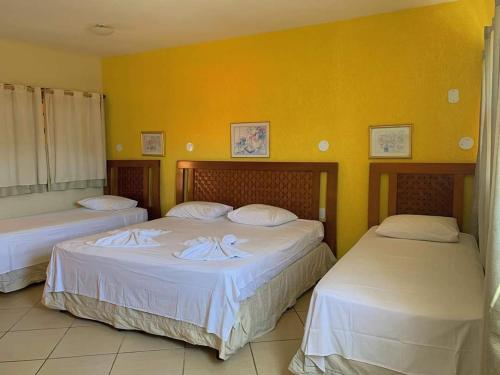 two beds in a room with yellow walls at Pousada Enseada da Vila in Cabo Frio