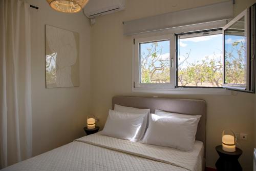Un dormitorio con una cama con almohadas blancas y dos ventanas. en Oinopia Apartments, en Aegina Town