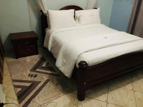 a bed with white sheets and pillows and a night stand at Gorilla Homestay Kabale in Kabale