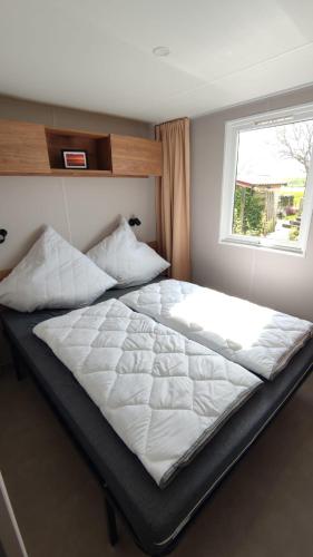a large bed in a bedroom with a window at MOBILHEIM HERZ LAUWERSOOG - Chalet Pampusplaat in Lauwersoog