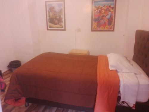 1 dormitorio con 1 cama marrón y 2 cuadros en la pared en Hostal festival, en Ollantaytambo