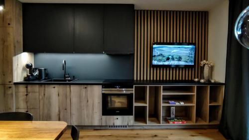 a kitchen with black cabinets and a tv on the wall at Moderní rodinný 3KK apartmán D8 v centru Harrachova s výhledem na skokanské můstky - by Relax Harrachov in Harrachov