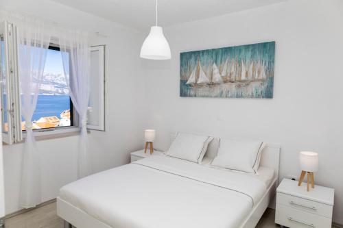 a white bedroom with a bed and a window at Holiday house Mila in Postira