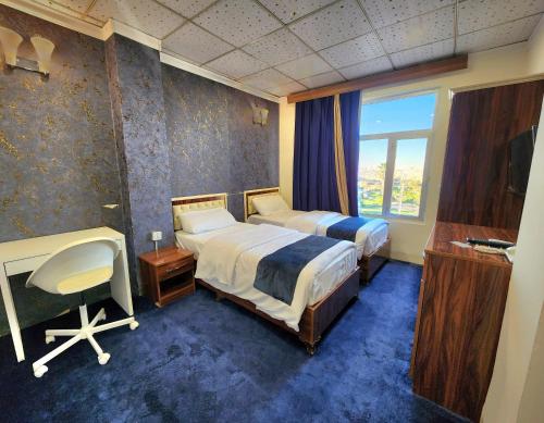a bedroom with two beds and a desk and a window at Vote Hotel in Erbil
