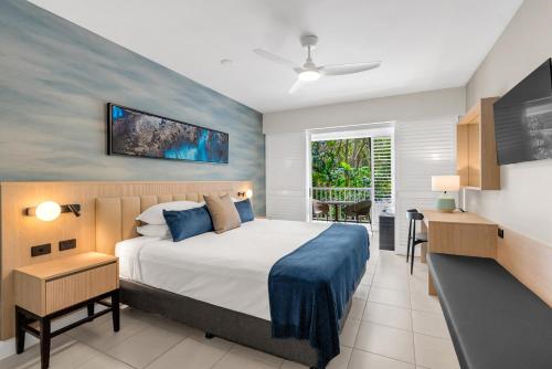 a bedroom with a bed and a desk and a window at Elysium The Beach Club in Palm Cove