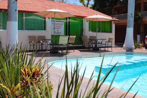 a swimming pool with tables and chairs and umbrellas at Hotel La Quinta Posada Real in Culiacán