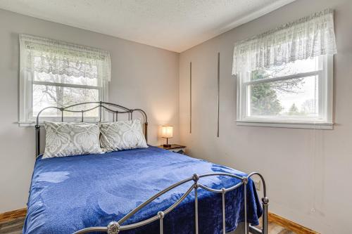 a bedroom with a bed with a blue comforter and two windows at Quaint Economy Retreat with Patio and Spacious Yard! 