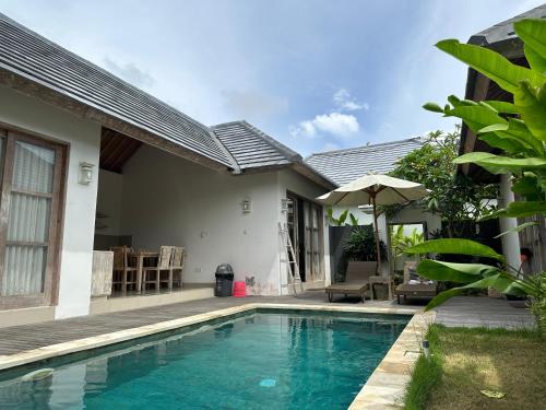 a swimming pool in front of a house with an umbrella at Bingin Garden Uluwatu in Uluwatu