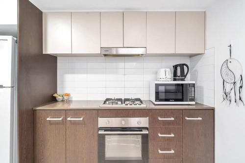 a kitchen with white cabinets and a stove and microwave at 'The Abstract at Kingsford' Spacious and Sunny Stay in Sydney