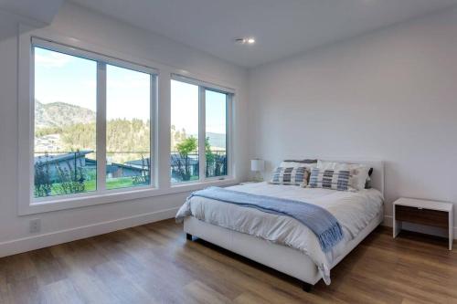 a white bedroom with a bed and large windows at Luxury Golf Stay w/Hot Tub in Kelowna
