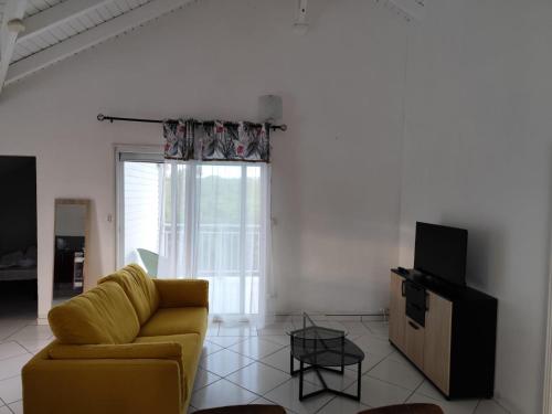 a living room with a yellow couch and a television at La pause marie-galantaise in Capesterre