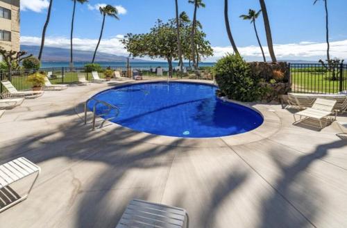 a large swimming pool with chairs and palm trees at Kanai A nalu in Wailuku