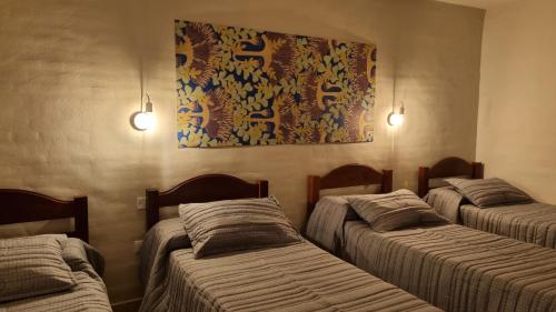 Habitación con 3 camas y una pintura en la pared. en Hotel Hualum en Villa Dolores