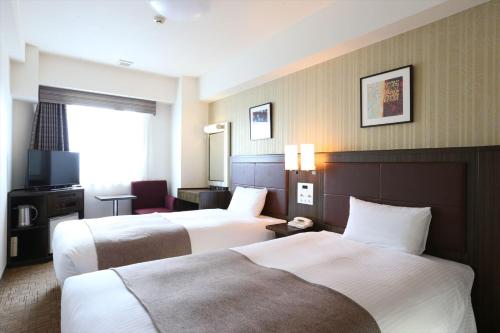 a hotel room with two beds and a television at Hotel Hokke Club Niigata Nagaoka in Nagaoka