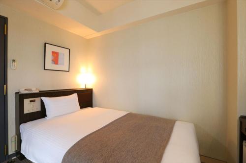a bedroom with a bed and a light on the wall at Hotel Hokke Club Niigata Nagaoka in Nagaoka