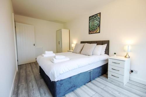 um quarto com uma cama grande com lençóis brancos e uma cómoda em Stylish 2BR Retreat - Near Station, Free Parking em Raynes Park