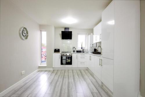uma cozinha branca com armários brancos e piso em madeira em Stylish 2BR Retreat - Near Station, Free Parking em Raynes Park