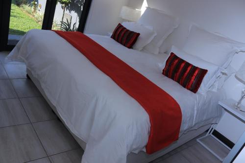 uma cama grande com lençóis e almofadas vermelhos e brancos em No 2 on Cladon Jadde Apartments em Chartwell